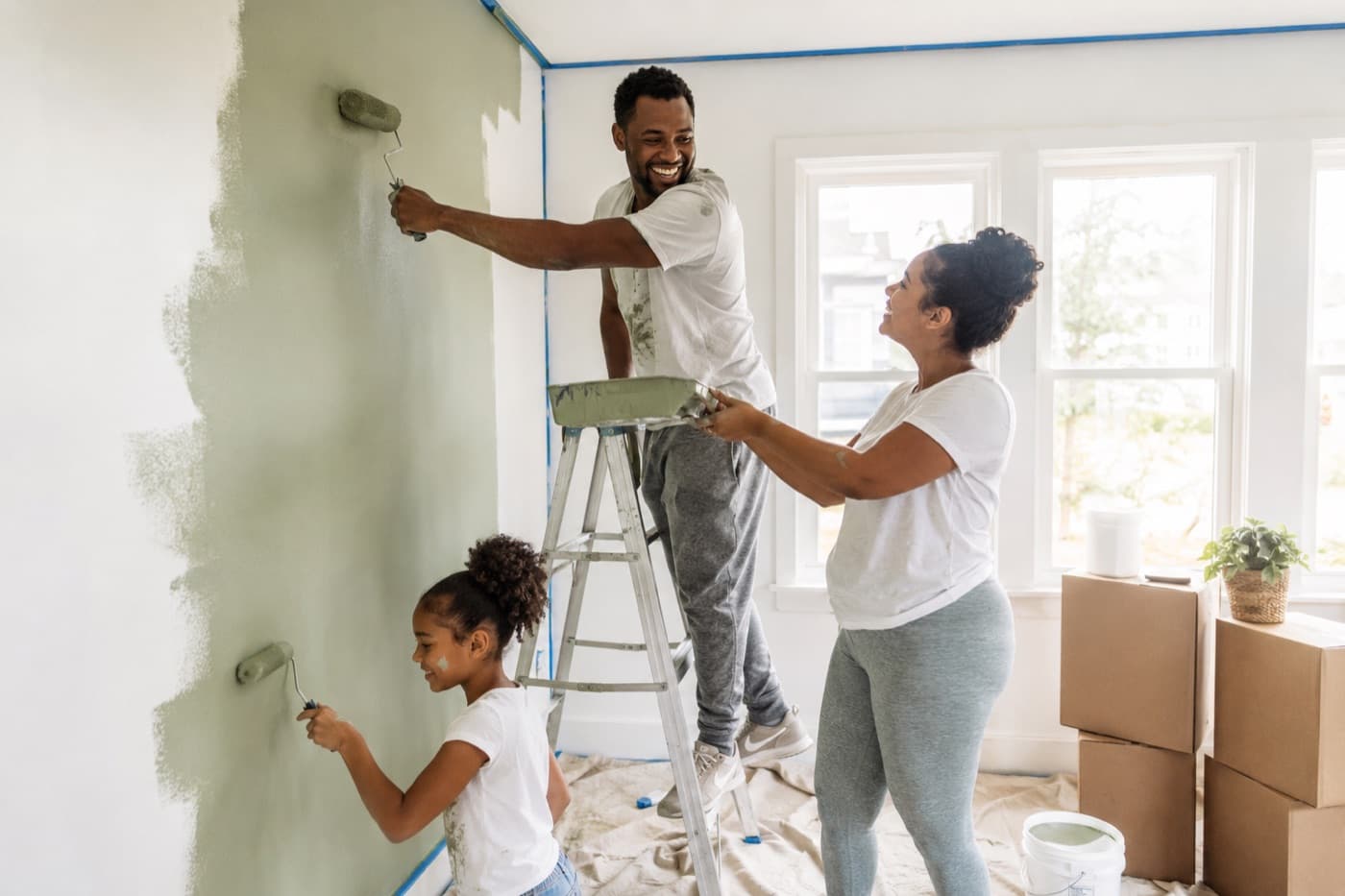 A family painting the living room of their new home together, their daughter rolling paint on the lowest part of the wall