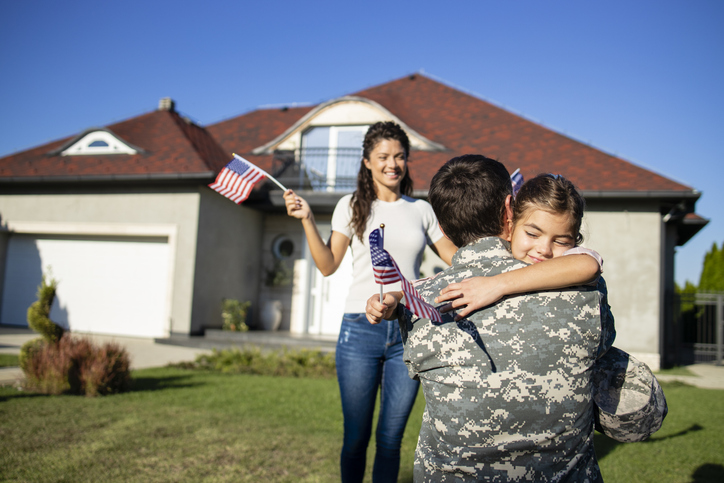 Little girl running to her dad soldier coming home from war and his beautiful wife waving American flags.